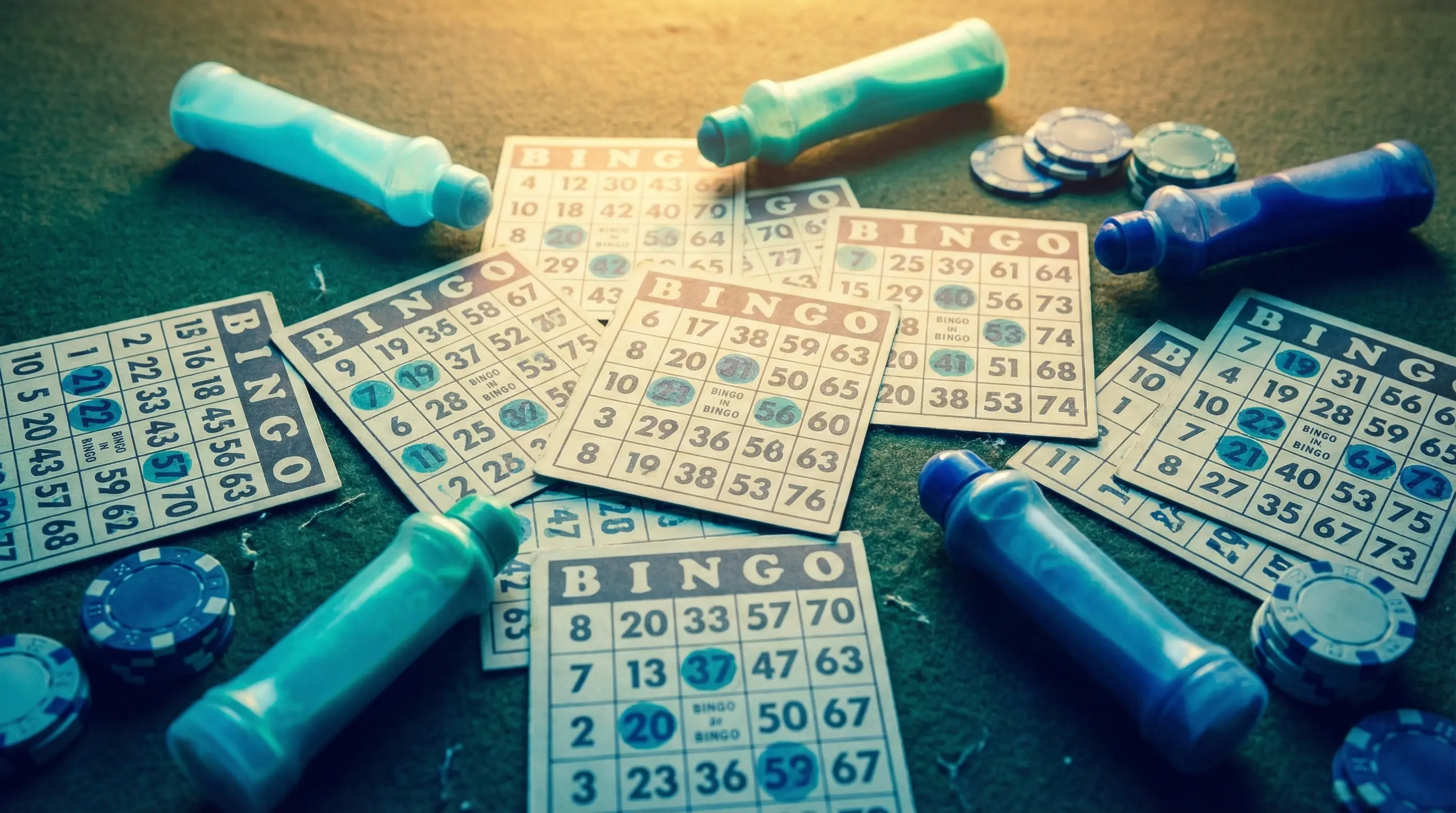 Bingo-Karten mit bunten Markern auf grünem Tisch von oben